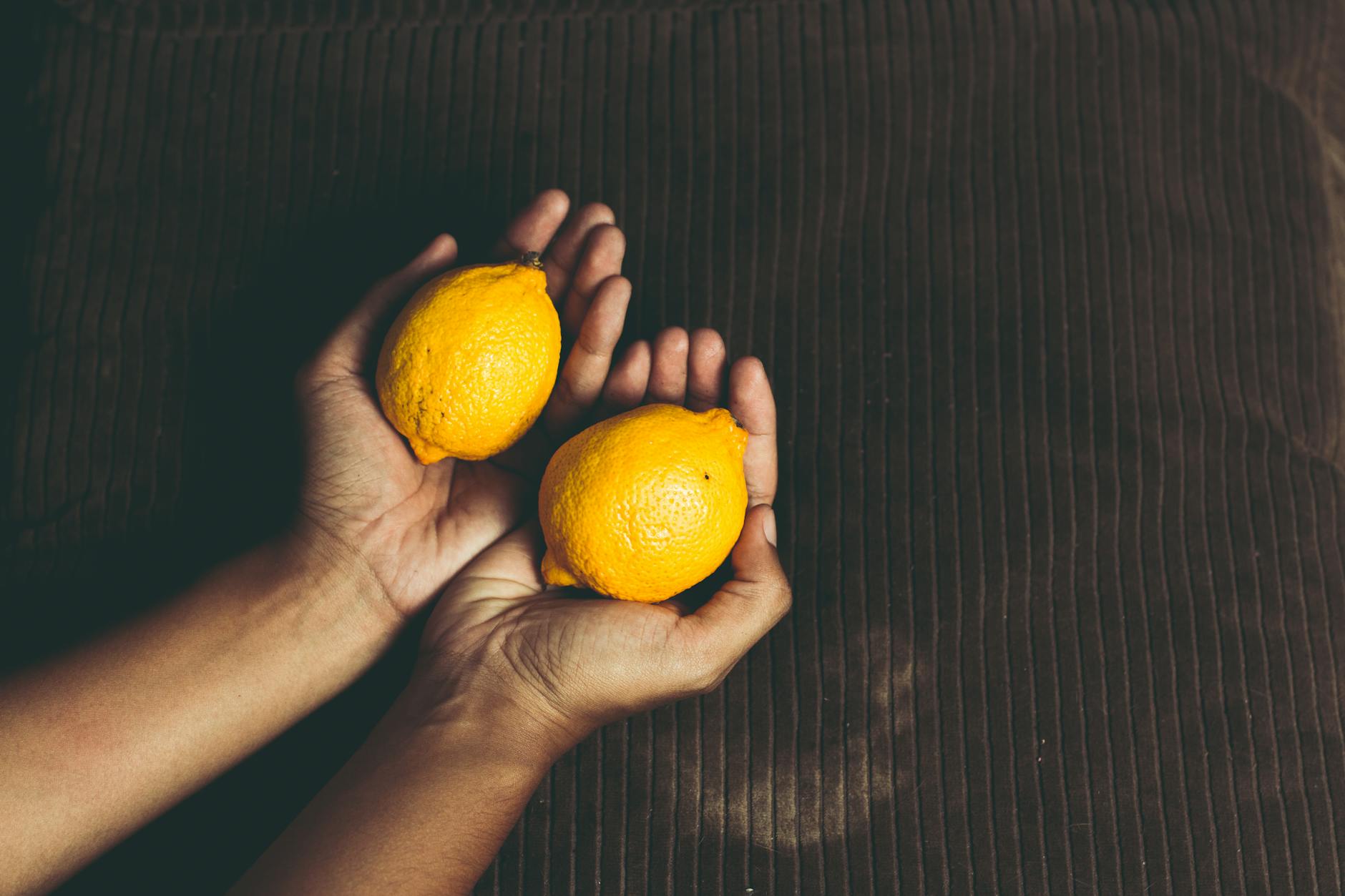 Two fresh lemons held in cupped hands on a brown surface, symbolizing sensitivity and care