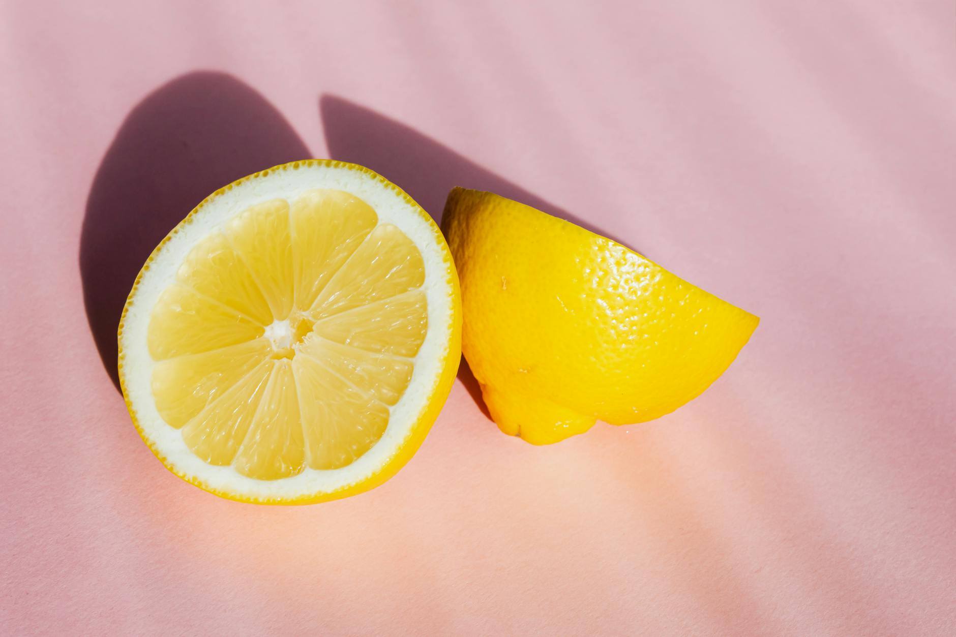 Limoni freschi tagliati a metà su sfondo rosa con raggi di sole, simbolo di freschezza e sensorialità