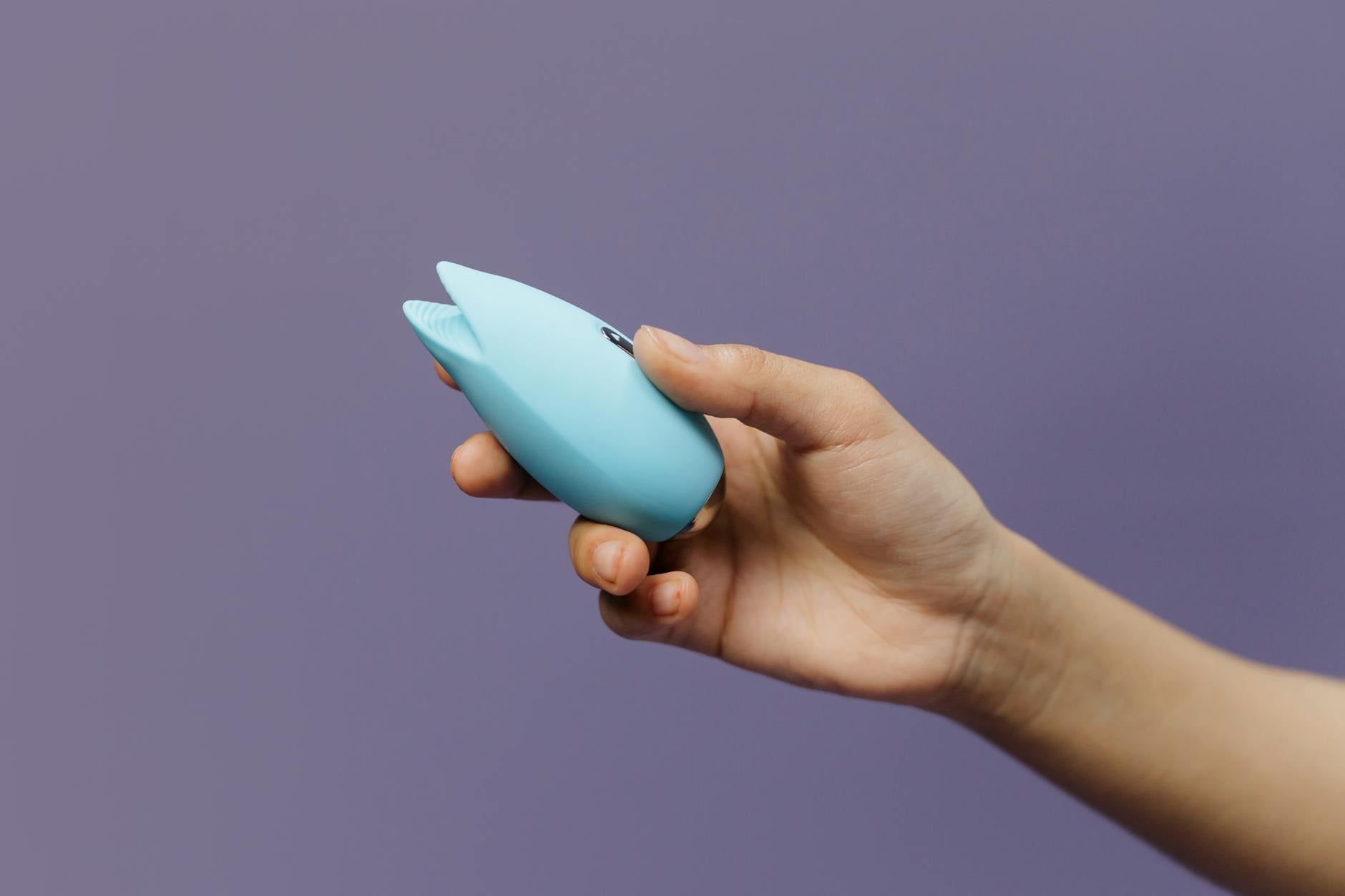 Hands holding a blue silicone lemon vibrator against a purple background, symbolizing self-love and shared pleasure