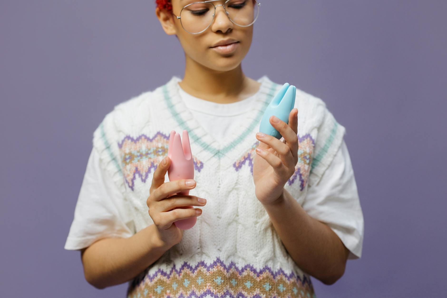 Woman holding blue and pink silicone vibrators while considering pleasure options with chronic pain