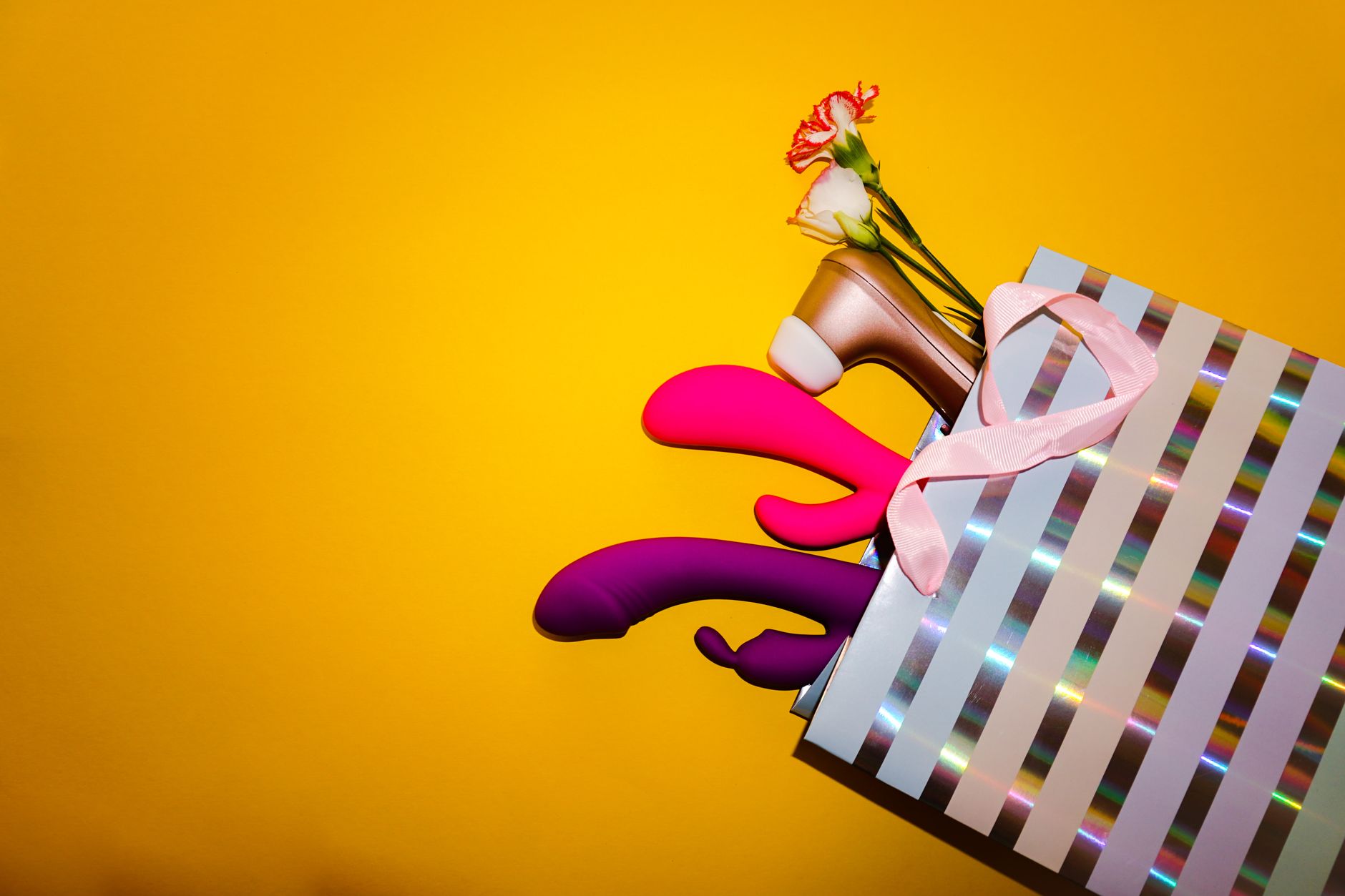 Colorful arrangement of vibrators and flowers on a bright yellow background showcasing various toy designs